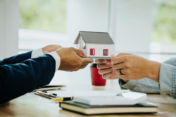 Two people exchanging house keys and signing documents, symbolizing home buying, mortgage,...