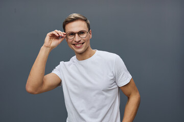 Smiling young man with glasses in casual white t-shirt adjusting his spectacles and looking at...