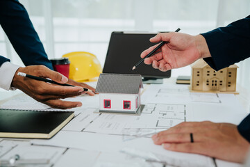 Team of architects and engineers collaborating at an office desk, reviewing blueprints and project plans for a building construction design.