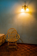 Cane chair against a wall with old world wallpaper and lamp