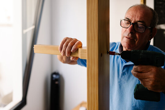 Elderly man operating a power drill to put together new furniture