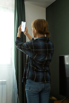 Woman searching for phone signal near window in living room