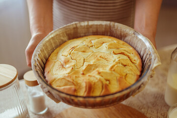 A cook's hands, wearing a striped apron, present a freshly baked apple pie in a glass dish.