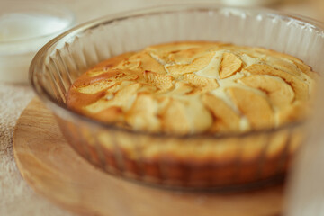 A close-up shows a freshly baked apple pie in a glass dish on a wooden surface.