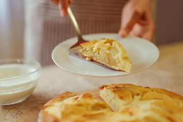 A cook in a striped apron uses a spatula to place a slice of freshly baked apple pie onto a white plate.