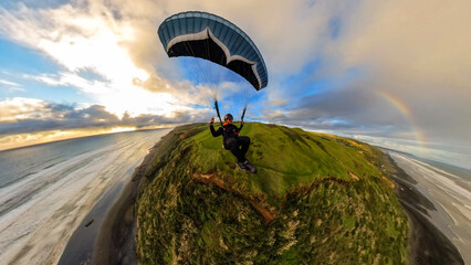 Extreme paragliding pilot soaring in the New Zealand beach at sunset. Adventure concept