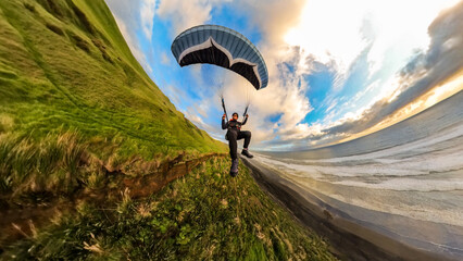 Extreme paragliding pilot soaring in the New Zealand beach at sunset. Adventure concept