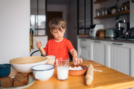Naklejki Toddler playing with flour and preparing dough for baking a cake