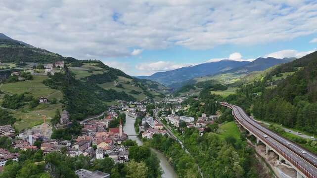 Drone footage captures Monastero di Sabo in Italy, with a valley, small town, river, winding roads, and mountains, showcasing natural beauty and historical charm