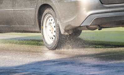 A car is driving on a wet road with water splashing out from the back
