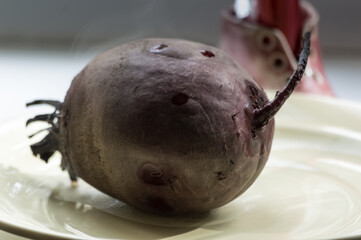 Boiled beetroot on a plate on a light background. Warm steam comes from the beetroot. Selective focus. Toned.