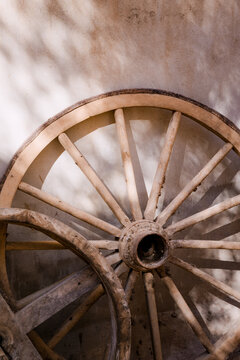 An old wooden wheel leaning against a sunlit wall