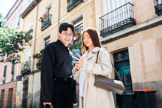 Young couple using smartphone while walking down urban street