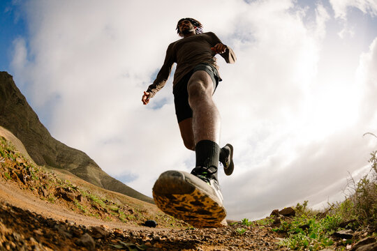 Wide low-angle shot of a professional runner jogging on a rocky trail