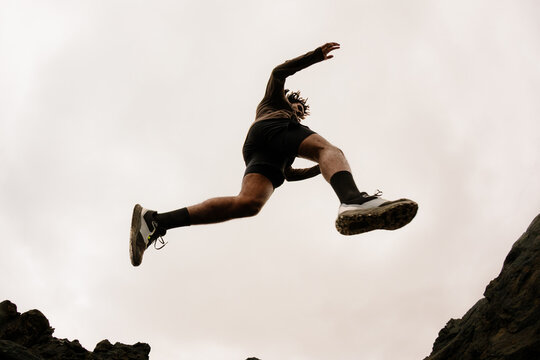 Wide shot of a person leaping over rocks with arms bent