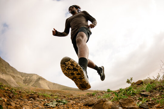 Wide shot from low angle of a runner crossing a rocky trail