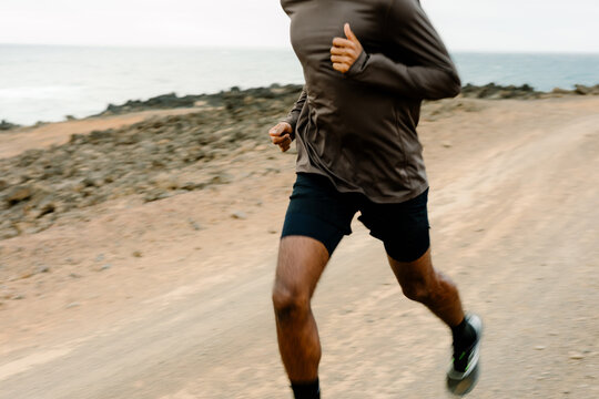 Anonymous man runs alone on a dusty trail near a volcanic coastline