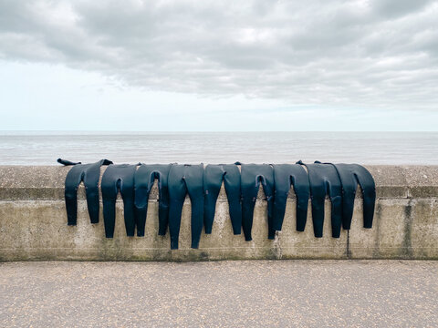 A line of wetsuits drying on a wall