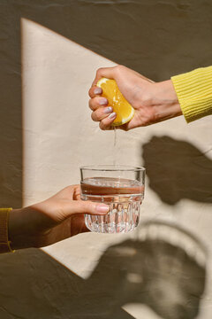 Squeezing Lemon Juice Into a Glass of Water in Sunlit Setting