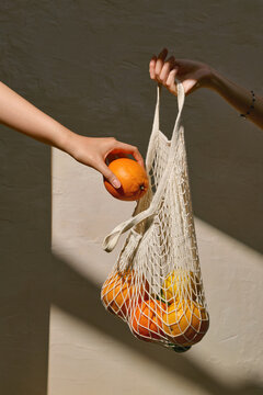 Hands Holding a Net Bag Filled With Fruits in Warm Sunlight