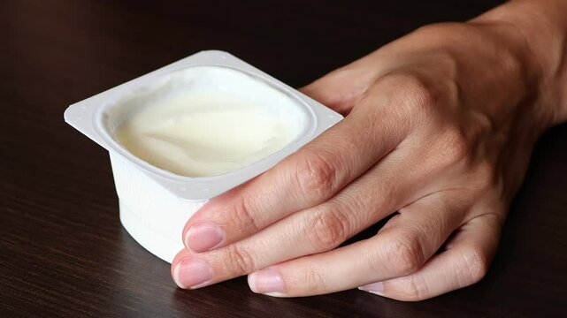 Close up view of plain greek yogurt in a plastic cup. Woman's hands scooped yoghurt with silver spoon. Concept of diet for weight loss, detox.