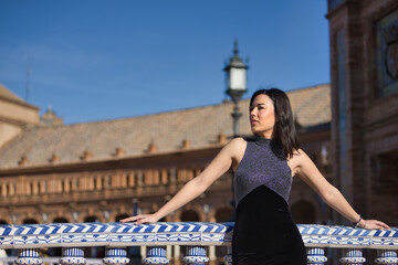 Young, beautiful, brunette woman in a fancy black dress, looking at infinity, leaning on a tiled...