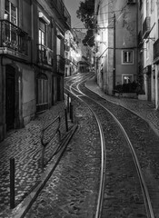 Black and white street photography Lisbon tram rails historic cobblestone alley night travel photo vintage architecture moody cityscape artistic monochrome Portugal old town charming journey