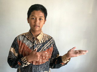 A teenage boy wearing a batik shirt pointing to the side, isolated on white
