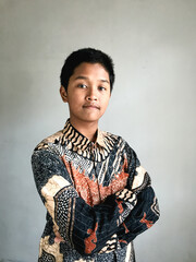 A teenage boy wearing a batik shirt posing confidently with arms crossed and a slight smile, isolated on white