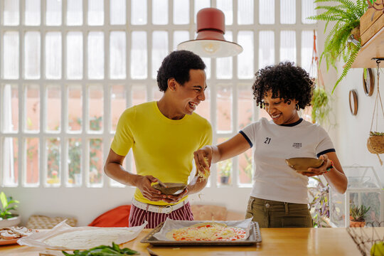 Flatmates making pizza together, adding cheese and having fun