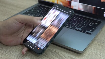 Person scrolling aimlessly on a mobile phone with a modern laptop in the background - Powered by Adobe