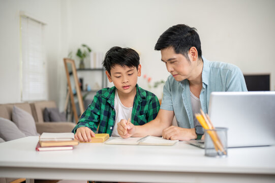 Father is holding a pencil and pointing in notebook while teaching a homework to his son.
