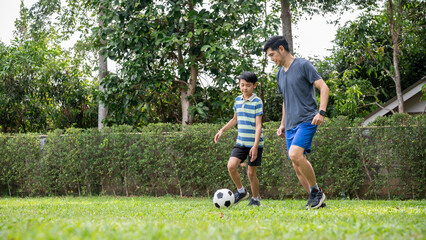 Father and a son playing football or soccer together in their home's backyard or a green grass field.
