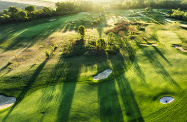 Golf course at sunset with beautiful sky and sand trap. Scenic panoramic view of golf fairway with bunker from drone