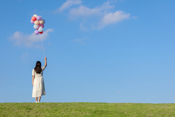 The back view of a Chinese woman holding a bunch of balloons on the grass