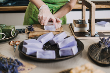 Person slices lavender soap bars by hand in a home soap studio filled with artisan tools and...