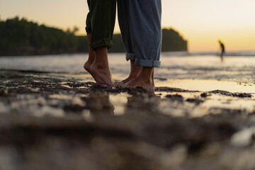 Barefoot couple standing close together on the beach at sunset