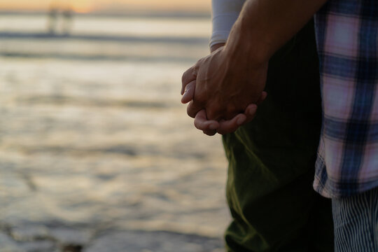 Close-up of couple holding hands at the beach during sunset