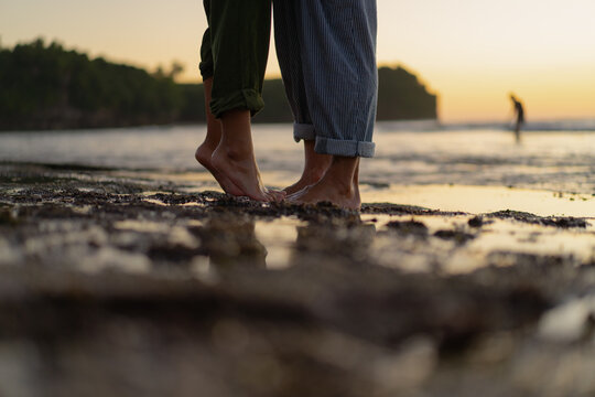 Barefoot couple standing close together on the beach at sunset