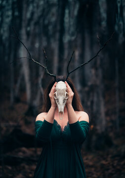 Woman posing with deer skull in front of face in dark forest setting.