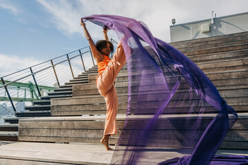 Woman lifting leg high with purple fabric on outdoor wooden steps