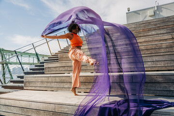 Woman kicking leg upward with flowing fabric on wooden steps