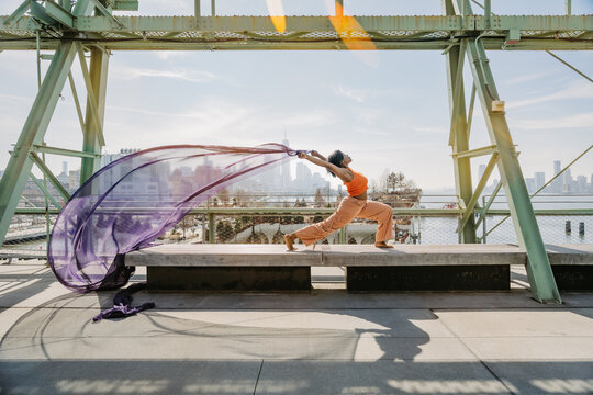 Woman lunging with purple fabric flowing on urban platform