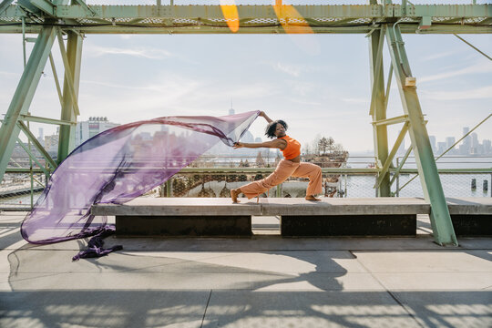 Woman striking dynamic pose with purple fabric over city backdrop