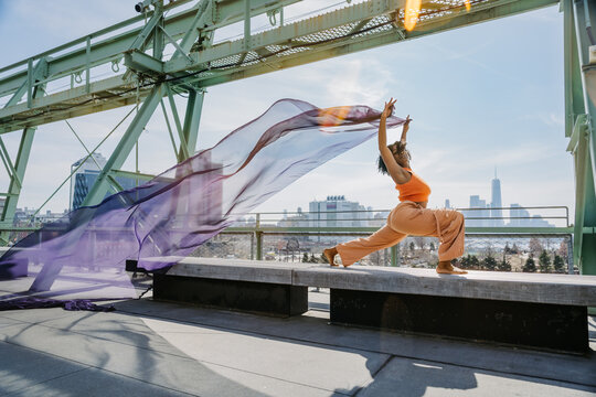 Woman lunges with arms raised, fabric trailing, NYC skyline behind