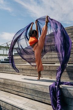 Woman holding vertical leg lift with flowing purple fabric outdoors