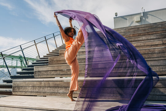 Woman lifting leg high with purple fabric on outdoor wooden steps