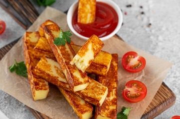 Fried halloumi cheese sticks with tomato sauce on a wooden board on a concrete background.