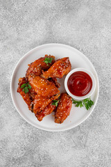 Baked chicken wings in a sweet chili sauce and sesame seeds on a white plate on a concrete background. Top view, copy space.