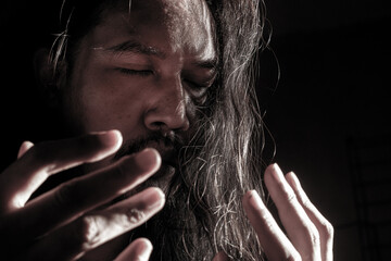 Long-Haired Man Praying Devoutly in Dimly Lit Room – Spiritual and Emotional Moment